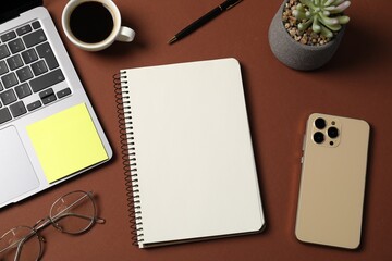 Notebook with pen, laptop, smartphone, sticky note and coffee on brown background, flat lay