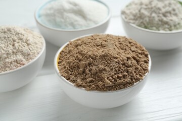 Different types of flour in bowls on white wooden table, closeup