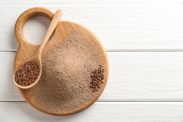 Flaxseed flour and spoon with seeds on white wooden table, top view. Space for text