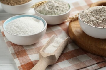 Different types of flour in bowls and scoop on table, closeup