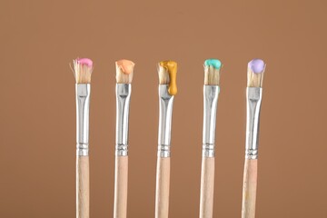 Many brushes with color paints on light brown background, closeup