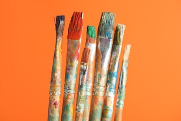 Many dirty paintbrushes on orange background, closeup
