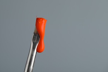 Brush with orange paint on light grey background, closeup. Space for text
