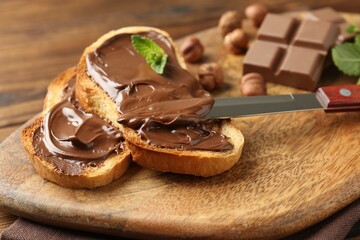 Toasts with tasty chocolate spread, pieces, mint and hazelnuts on table, closeup