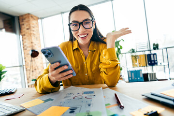 Young businesswoman in a bright modern office using a smartphone cheerfully, showcasing a...