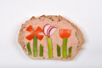 A slice of bread covered with pate is creatively garnished with sliced vegetables to depict flowers...