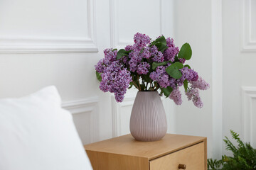 Bouquet of beautiful lilac flowers on wooden table near white wall