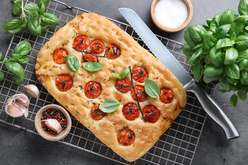 Delicious focaccia with tomatoes, spices and knife on gray textured table, flat lay