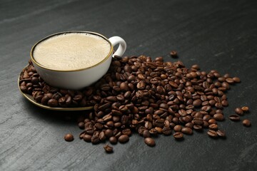 Aromatic coffee in cup and beans on black table, closeup