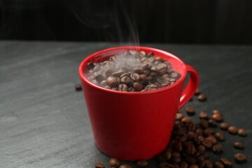 Aromatic coffee beans in cup on black table, closeup
