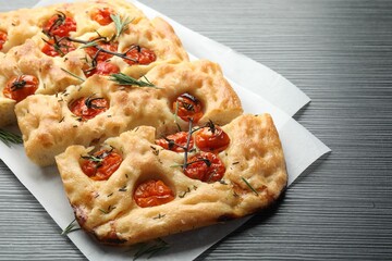 Cut delicious focaccia with tomatoes and spices on dark wooden table, closeup