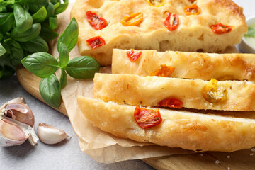 Cut delicious focaccia with tomatoes and spices on gray table, closeup