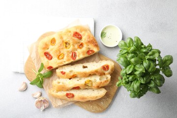 Cut delicious focaccia with tomatoes, spices and oil on gray table, flat lay