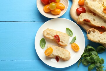 Pieces of delicious focaccia with tomatoes and basil on light blue wooden table, flat lay. Space for text