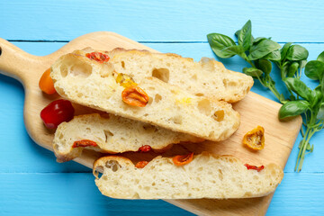 Pieces of delicious focaccia with tomatoes and basil on light blue wooden table, flat lay
