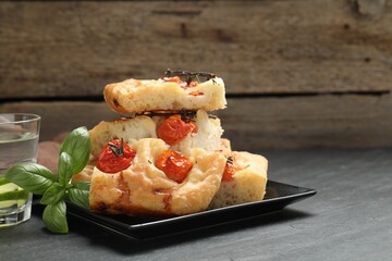 Pieces of delicious focaccia with tomatoes, basil and glass of water on gray table