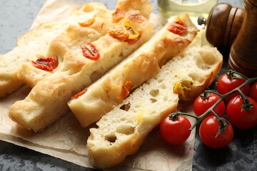 Pieces of delicious focaccia with tomatoes, spices and oil on table, closeup