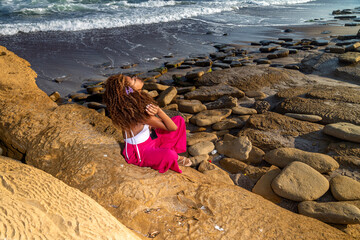 Young woman relaxing on rocky beach at sunset during adventure trip