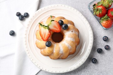 Tasty Bundt cake with powdered sugar and berries on light grey table, flat lay