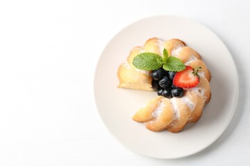 Tasty bundt cake with powdered sugar, berries and mint on white table, top view. Space for text