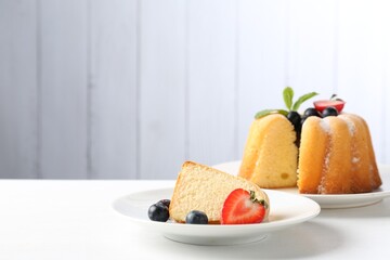 Tasty bundt cake with powdered sugar, berries and mint on white table, closeup. Space for text