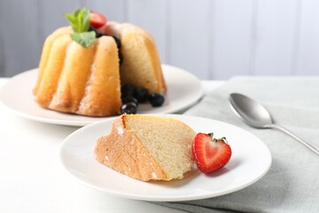 Tasty bundt cake with powdered sugar, berries, mint and spoon on white table, closeup