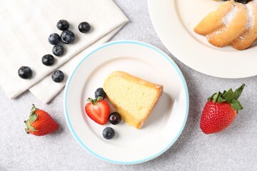 Tasty bundt cake with powdered sugar and berries on light grey table, flat lay