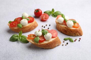 Tasty sandwiches with mozzarella cheese balls, tomato and basil on light grey table