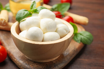Tasty mozzarella cheese balls, breadsticks, tomatoes and basil on wooden table, closeup