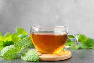 Aromatic lemon balm tea in glass cup and fresh leaves on gray textured table