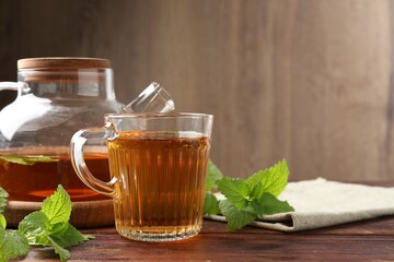 Aromatic lemon balm tea in glass cup, teapot and fresh leaves on wooden table, space for text
