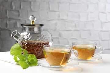 Aromatic lemon balm tea in glass cups, teapot and fresh leaves on white table