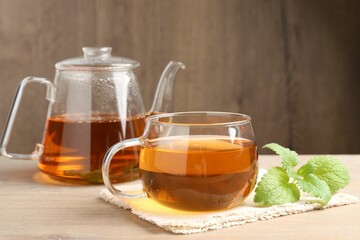 Aromatic lemon balm tea in glass cup, teapot and fresh leaves on wooden table