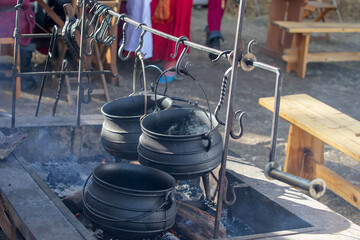 Traditional cast iron pots and kettle hanging over an open fire pit with rising smoke at outdoor...