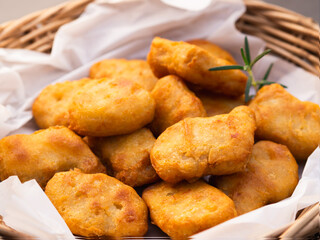 Crispy fried chicken nuggets and rosemary in basket with parchment paper.