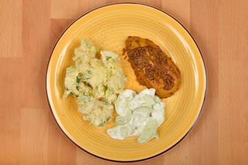 A yellow plate features a vegan imitation of chicken breast, potato salad, and cucumber salad