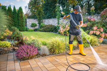 Gardener Uses Pressure Washer to Clean Patio in Lush Garden During Sunny Afternoon