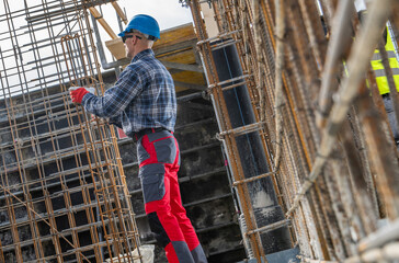 Construction Worker in Safety Gear Engages in Reinforcing Steel Structures at a Construction Site Near a Urban Environment in Midday Sunshine