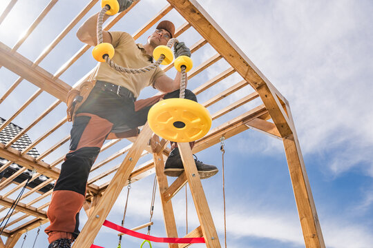 Construction of a Wooden Playground Structure With a Man Installing Yellow Rope Grips in Bright Daylight