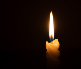 A single burning candle flame or light glowing on a spiral white candle on black or dark background...