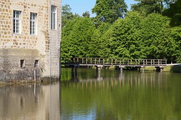 Wooden bridge crossing the moat of a medieval castle surrounded by lush trees