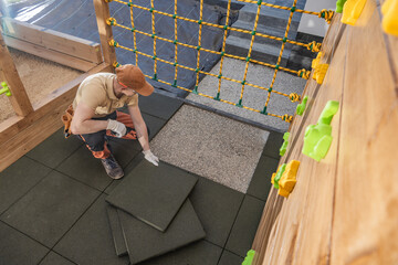 Worker Installs Safety Flooring in a Children's Play Area in a Recreational Facility During...