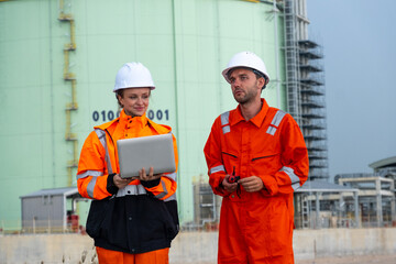 Workers in safety gear collaborate on a project near an industrial facility during daylight hours
