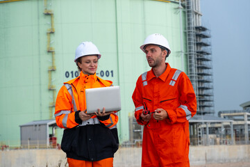 Two engineers in safety gear using a laptop at an industrial facility in the afternoon light