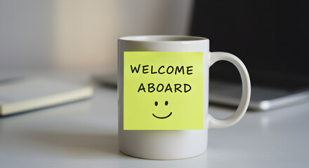 White Mug Featuring Yellow Sticky Note with Welcome Aboard Message on a Bright Office Desk with Laptop