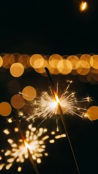 Sparkler emitting bright sparks with blurred golden bokeh lights in the dark background