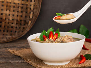 Use spoon to pick up chicken green curry in white bowl on wooden table background. Thai Food