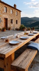 Fototapeta premium Long wooden table is beautifully set for dinner with plates and glasses, surrounded by olive trees as the sun sets warmly