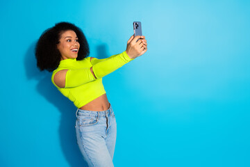 Young African American woman in vibrant green top taking a selfie with cheerful expression, posing against a blue background