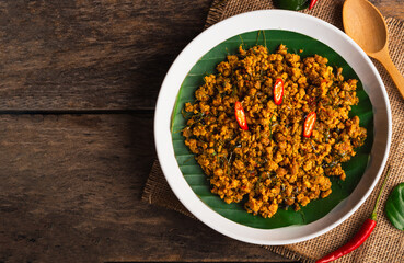 Top view of stir fried pork with yellow curry paste in white plate on wooden table background. Traditional Thai southern food
